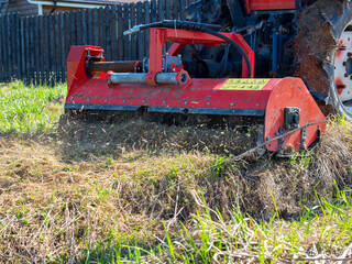 a tractor with a mower attached mulches dry grass along the fence. Land plot processing