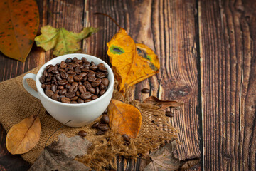 Cup of coffee beans and dry leaves on wooden floor, hello September concept.