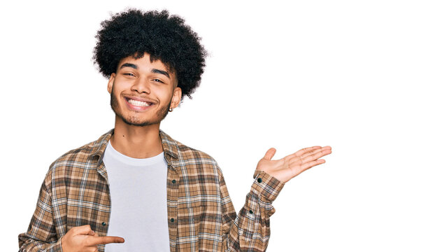 Young african american man with afro hair wearing casual clothes amazed and smiling to the camera while presenting with hand and pointing with finger.