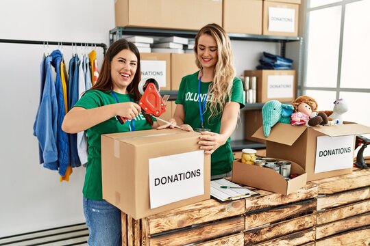 Two young volunteers woman smiling happy packing donations box at charity center.