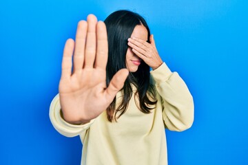 Young brunette woman wearing casual sweatshirt covering eyes with hands and doing stop gesture with...