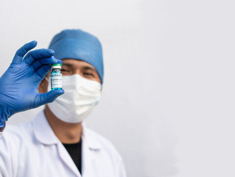 Hispanic Male Nurse Holding A Vial Containing A Blue Liquid, Covid19 Vaccine. Hispanic Man On White Studio.