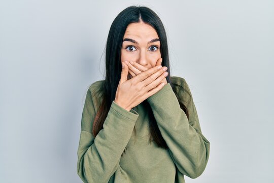 Young brunette woman wearing casual green sweater shocked covering mouth with hands for mistake. secret concept.