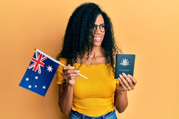 Middle age african american woman holding australian flag and passport smiling looking to the side...