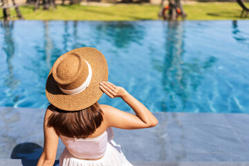 Fototapeta na wymiar Young woman traveler relaxing and enjoying by a tropical resort pool while traveling for summer vacation