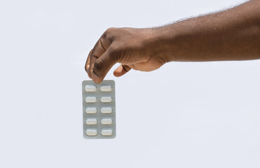 A hand holding a medicine pack with two fingers on isolated white background