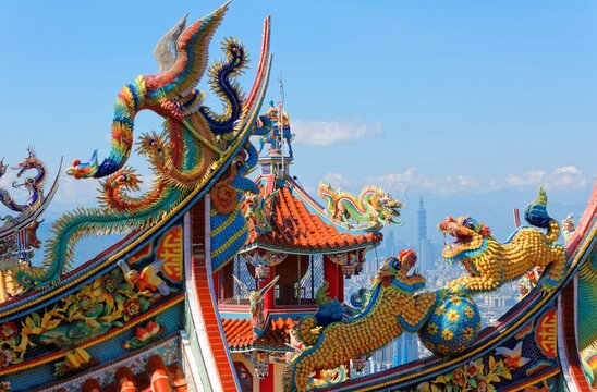 A Taiwanese temple decorated with sacred & auspicious animals (dragons & lions) on the roofs in traditional mosaic art & landmark 101 Tower standing out in background under sunny sky in Taipei, Taiwan