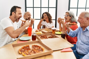 Group of middle age people smiling happy eating italian pizza sitting on the table at home