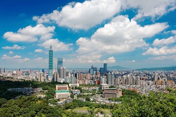 Fototapeta premium Aerial panorama of Downtown Taipei, vibrant capital city of Taiwan, with prominent Taipei 101 Tower among skyscrapers in Xinyi District & Yangmingshan Mountain on distant horizon under blue sunny sky