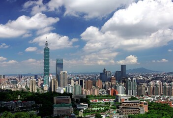 Naklejka premium Aerial panorama of Downtown Taipei, vibrant capital city of Taiwan, with prominent Taipei 101 Tower among skyscrapers in Xinyi District & Yangmingshan Mountain on distant horizon under blue sunny sky