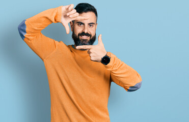Naklejka premium Hispanic man with beard wearing casual winter sweater smiling making frame with hands and fingers with happy face. creativity and photography concept.