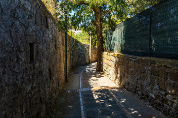 Very narrow street with high stony fences and a lot of shadows