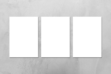 Three empty white vertical DIN A4 rectangle poster or business card mockups on the gray concrete stone wall.Flat lay, top view. For advertising, brand design, stationery presentation.