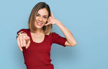 Young blonde girl wearing casual clothes smiling doing talking on the telephone gesture and pointing to you. call me.