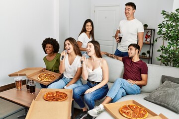Group of young friends having party eating italian pizza and singing song at home.