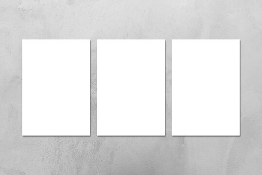 Three empty white vertical DIN A4 rectangle poster or business card mockups on the gray concrete stone wall.Flat lay, top view. For advertising, brand design, stationery presentation.