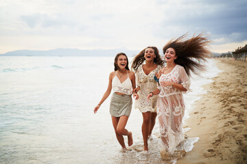 Three young cheerful women running and laughing on beach shore