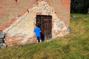 Obraz na płótnie Canvas Small kid checking an old wooden door. Back towards camera. Brick house. Summer time during the day, sunny weather outside. Concept of happiness. Copy space for extra text. Stockholm, Sweden, Europe.