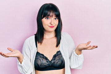 Young hispanic woman wearing lingerie clueless and confused expression with arms and hands raised. doubt concept.