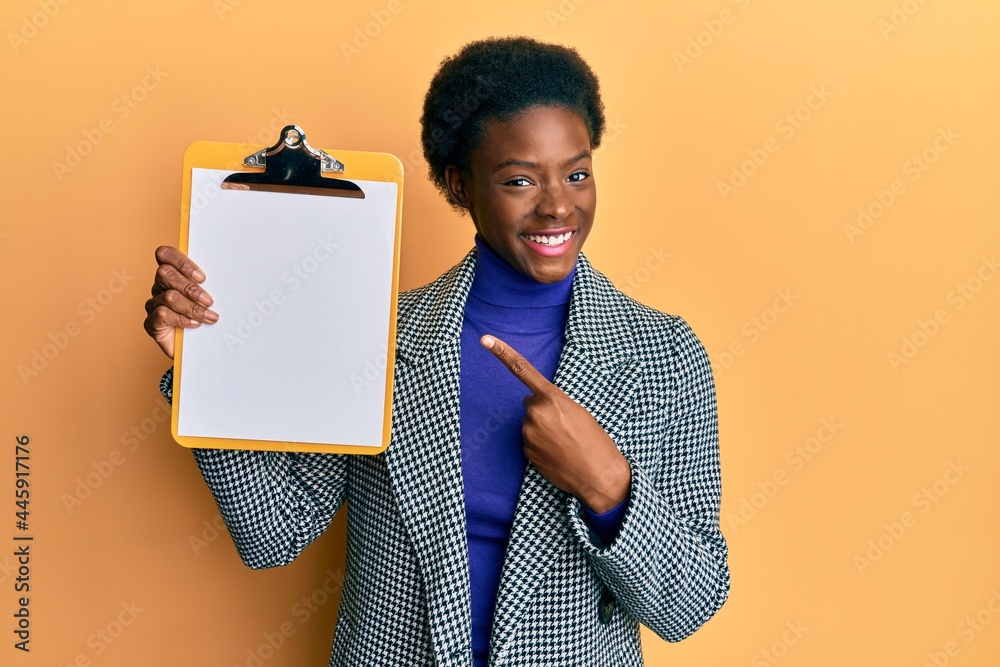 Poster Young african american girl holding clipboard with blank space smiling happy pointing with hand and finger