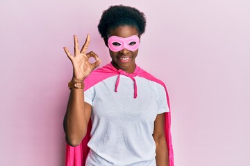 Young african american girl wearing superhero mask and cape costume smiling positive doing ok sign with hand and fingers. successful expression.