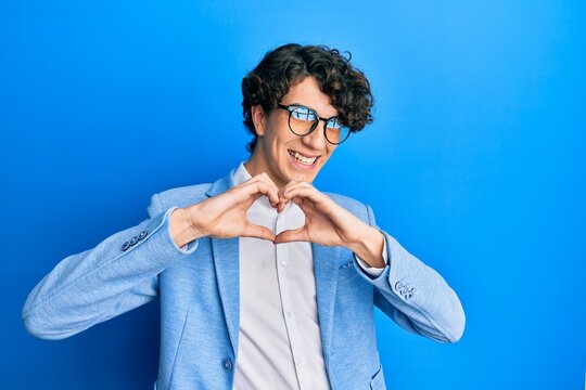 Hispanic young man wearing business jacket and glasses smiling in love showing heart symbol and shape with hands. romantic concept.