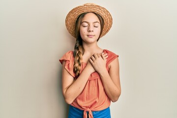 Beautiful brunette little girl wearing summer hat smiling with hands on chest with closed eyes and grateful gesture on face. health concept.