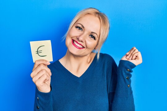 Young blonde woman holding euro symbol reminder screaming proud, celebrating victory and success very excited with raised arm