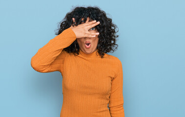 Fototapeta na wymiar Young hispanic woman wearing casual clothes peeking in shock covering face and eyes with hand, looking through fingers with embarrassed expression.