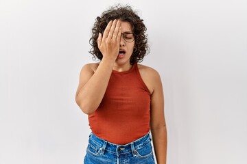 Young hispanic woman wearing glasses standing over isolated background yawning tired covering half face, eye and mouth with hand. face hurts in pain.