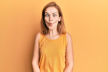 Young caucasian woman wearing casual style with sleeveless shirt making fish face with lips, crazy...