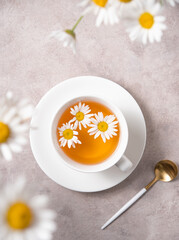 chamomile tea in a white cup with flowers daisy  on a pink-gray background. Top view and close up