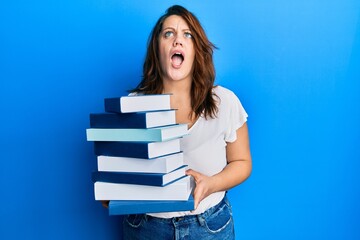 Young caucasian woman holding a pile of books angry and mad screaming frustrated and furious, shouting with anger looking up.