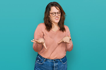 Young plus size woman wearing casual clothes and glasses disgusted expression, displeased and fearful doing disgust face because aversion reaction. - obrazy, fototapety, plakaty