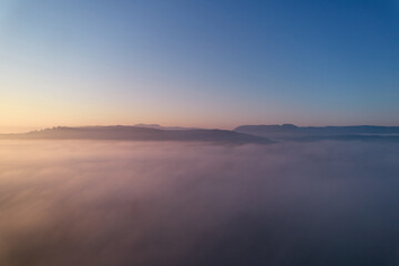 Fototapeta premium Landscape shot above the fog. Hill panorama of swabian alb on the horizon. Blue sky for copy space. Aerial view.