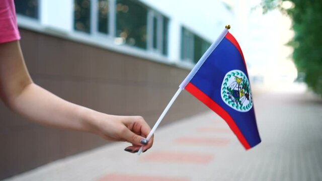 Unrecognizable woman holding Belizean flag. Girl walking down street with national flag of Belize