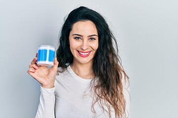 Young hispanic woman holding earwax cotton remover looking positive and happy standing and smiling with a confident smile showing teeth