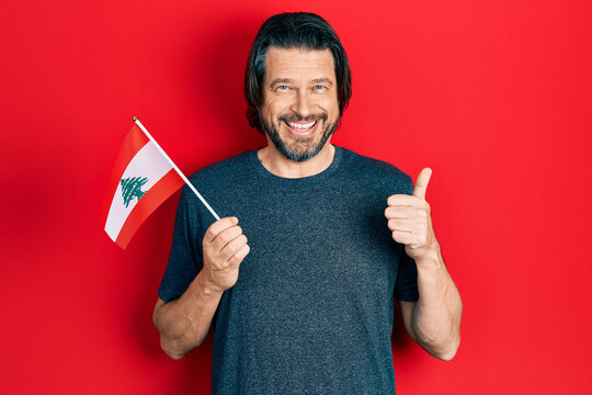 Middle age caucasian man holding lebanon flag smiling happy and positive, thumb up doing excellent and approval sign
