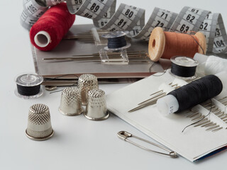 A pile of wooden buttons, a needle, old thimbles, scissors and a spool of cotton thread on a white background. The concept of needlework, sewing, tailoring
