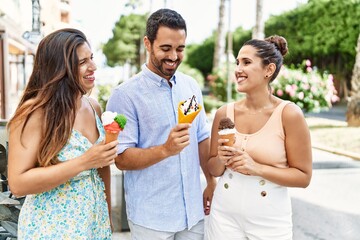 Three hispanic friends smiling happy eating ice cream at the city.