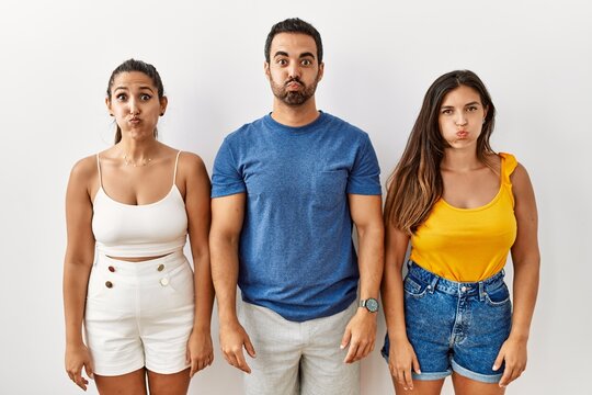 Group of young hispanic people standing over isolated background puffing cheeks with funny face. mouth inflated with air, crazy expression.