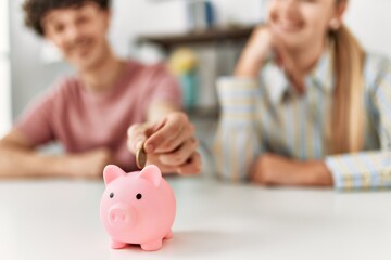 Young couple inserting coin inside piggy bank at home.