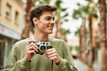 Young hispanic tourist man smiling happy using vintage camera at the city.