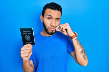 Hispanic man with beard holding italy passport mouth and lips shut as zip with fingers. secret and...