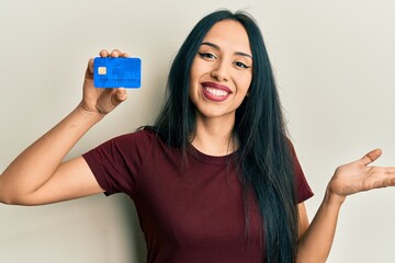 Young hispanic girl holding credit card celebrating achievement with happy smile and winner expression with raised hand