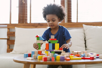 Little African american boy building a small house with colorful wooden blocks in living room at...