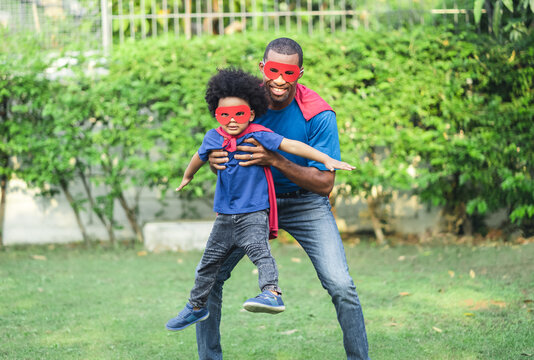 African Black Family Spent Time Together In The Home Garden. Laughing Father And Son Playing Superhero At The Day Time. Happy African American Family Life, Father Day Concept