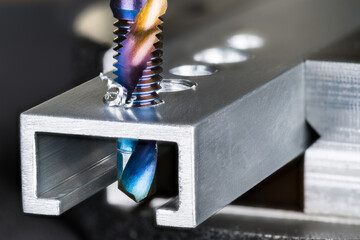 Closeup of tap and drill bit making a threaded hole in aluminum profile with metal shavings. Spiral...