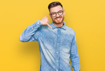 Young redhead man wearing casual denim shirt smiling doing phone gesture with hand and fingers like talking on the telephone. communicating concepts.