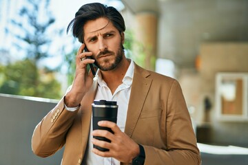 Young hispanic businessman talking on the smartphone and drinking coffee at the city.